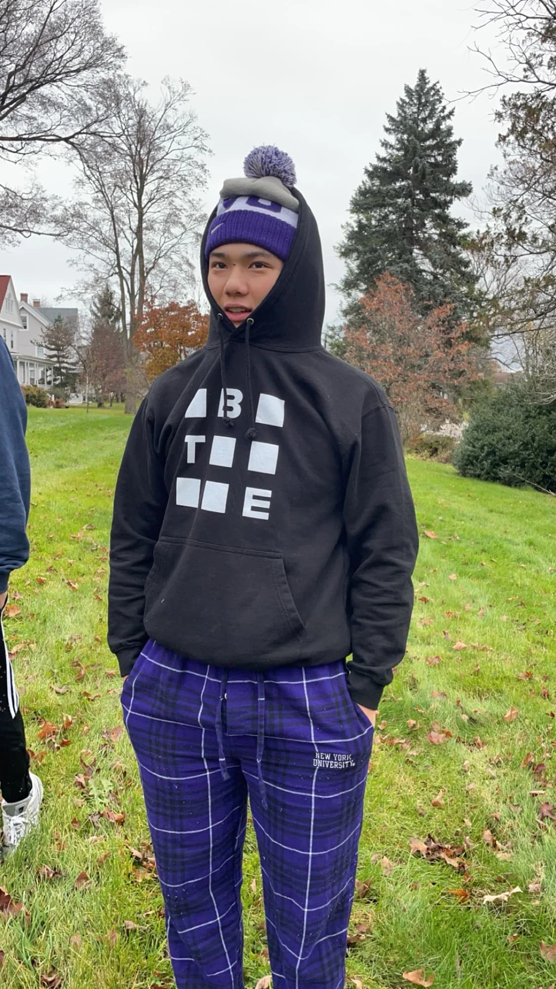 A member in an NYU beanie standing on a lawn