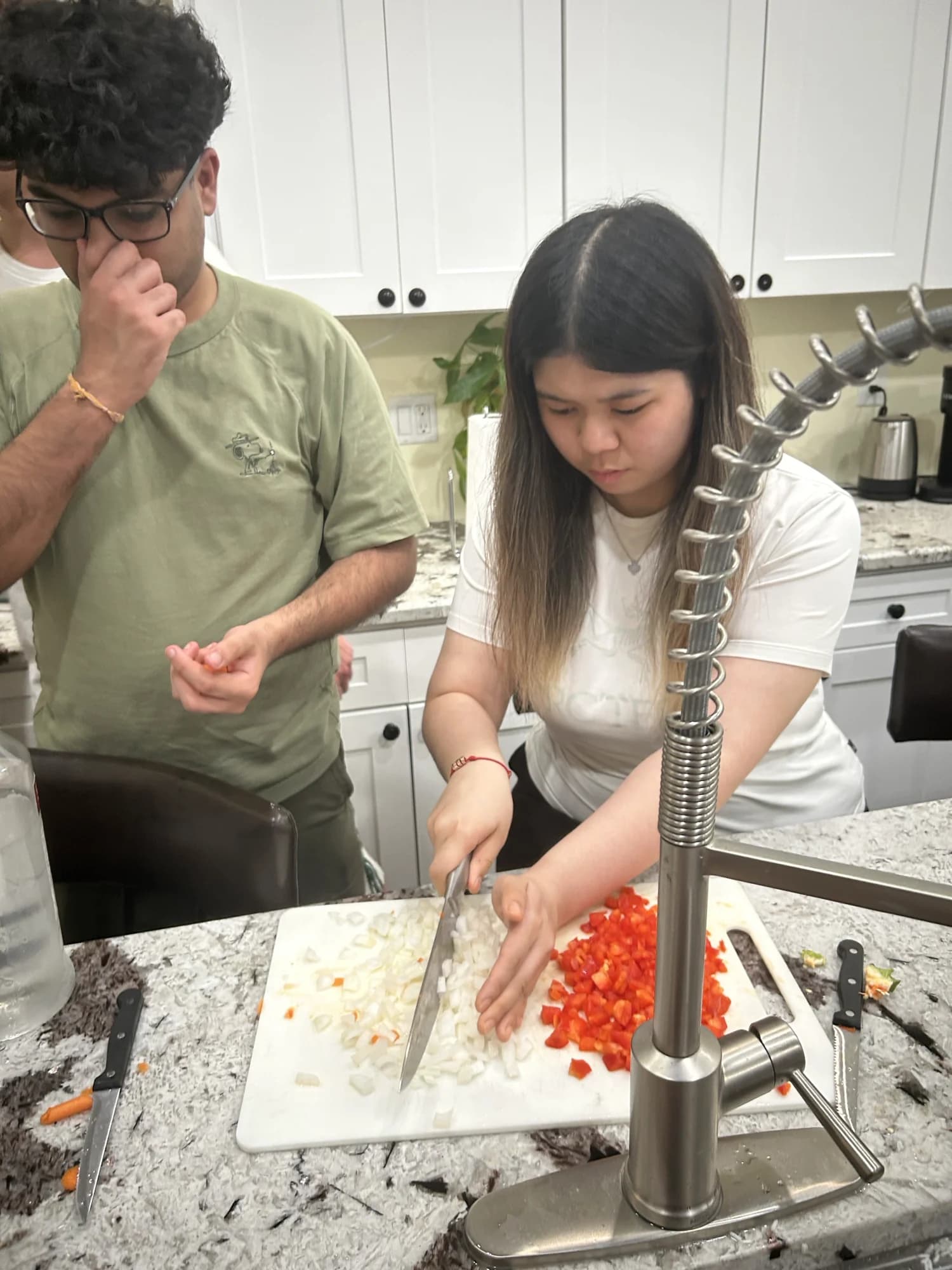 Two members chopping onions and peppers at a kitchen island