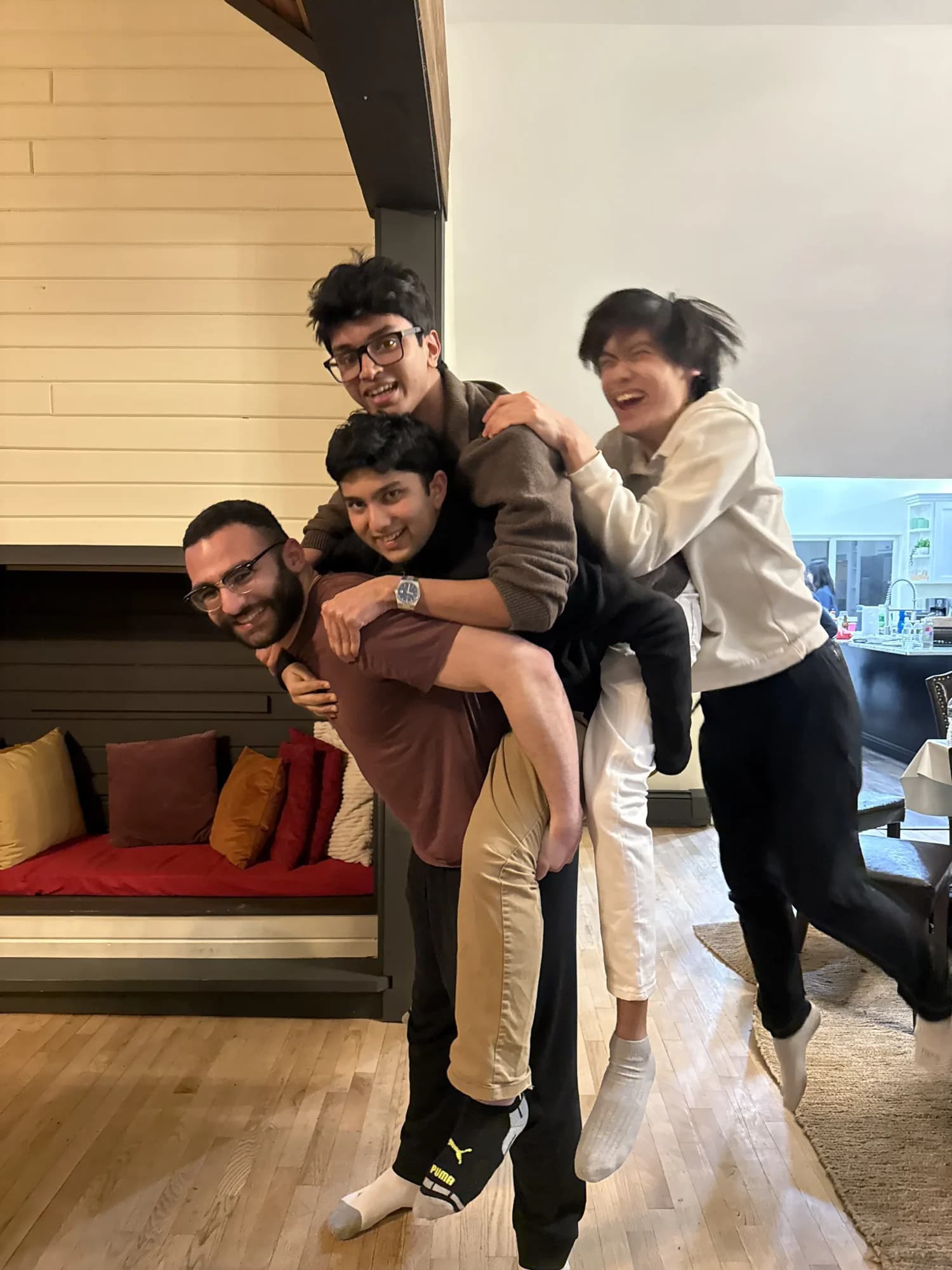 Three members climbing onto a fourth's back and shoulders in a living room
