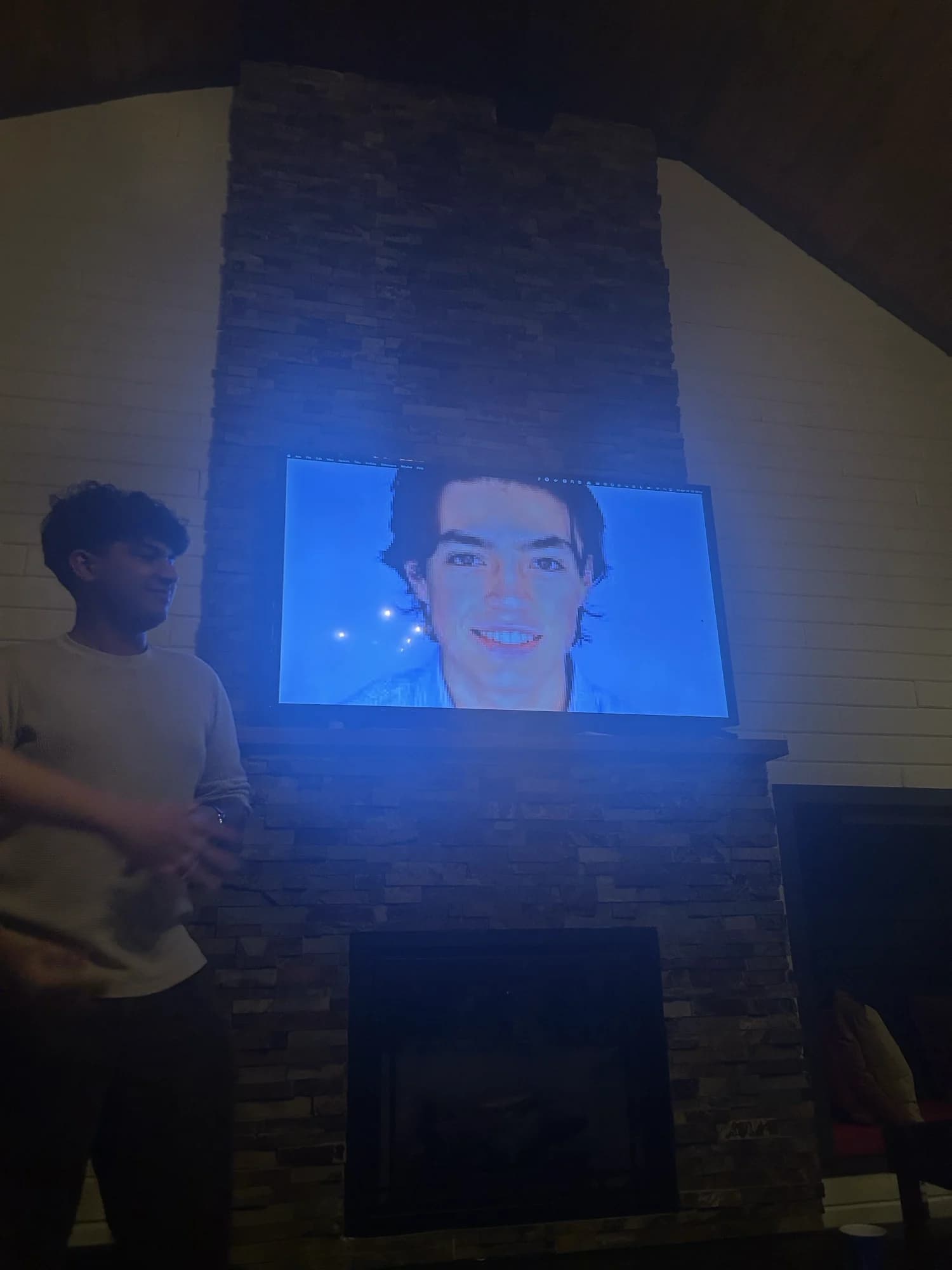 A member standing by a stone fireplace, a face frozen on the TV above it