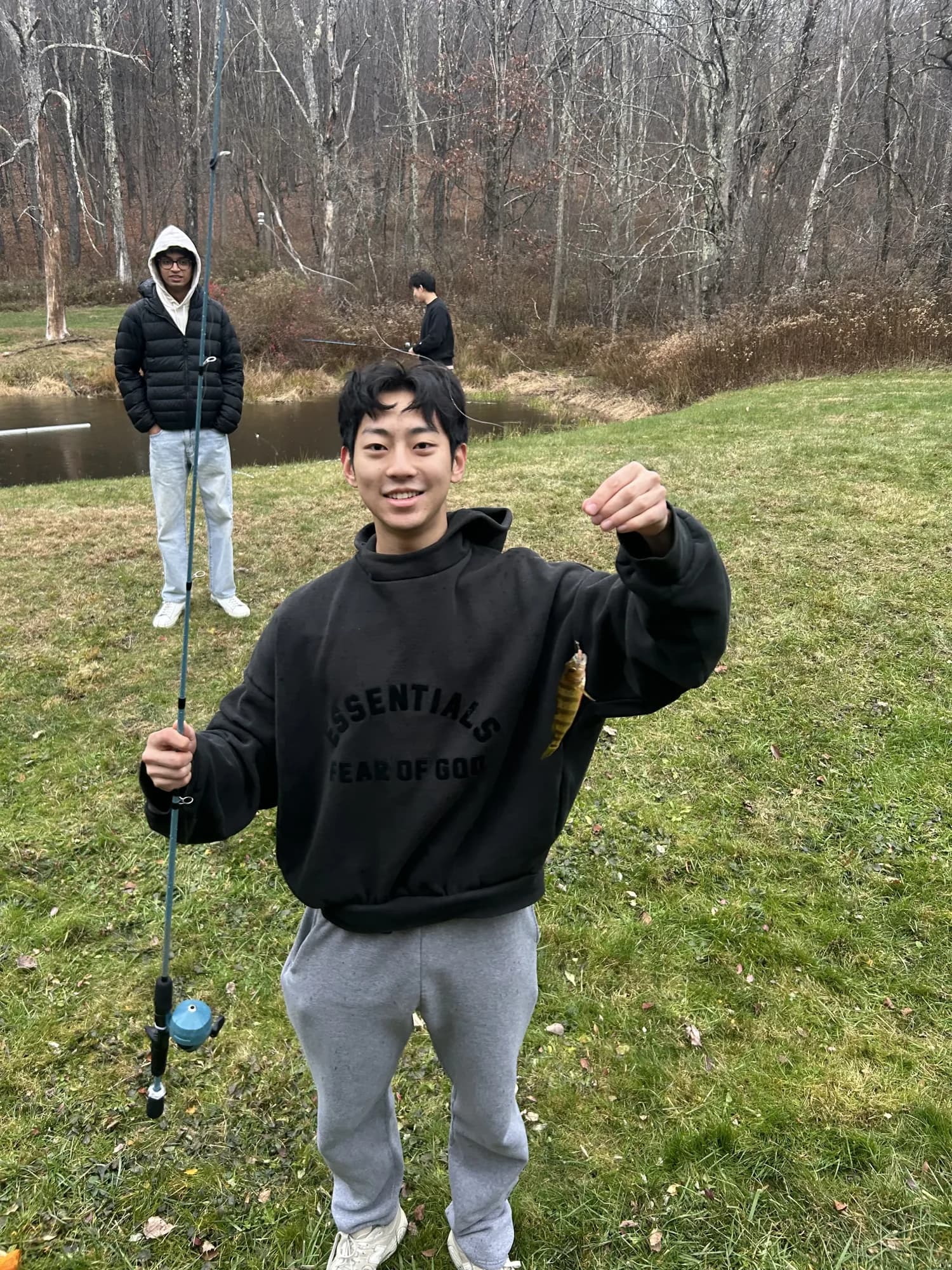 A member holding up a small fish he caught at a retreat, two members fishing behind him