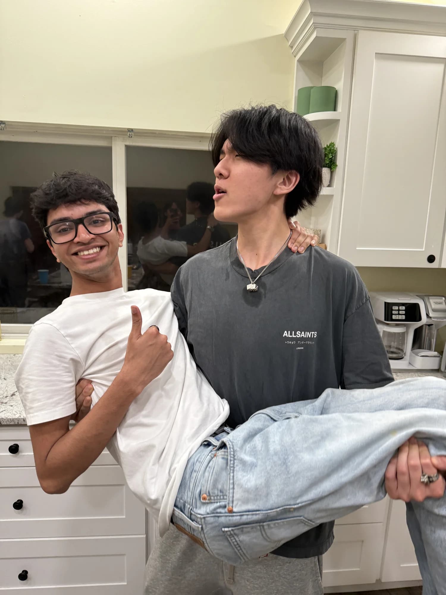 One member carrying another across a kitchen, both laughing