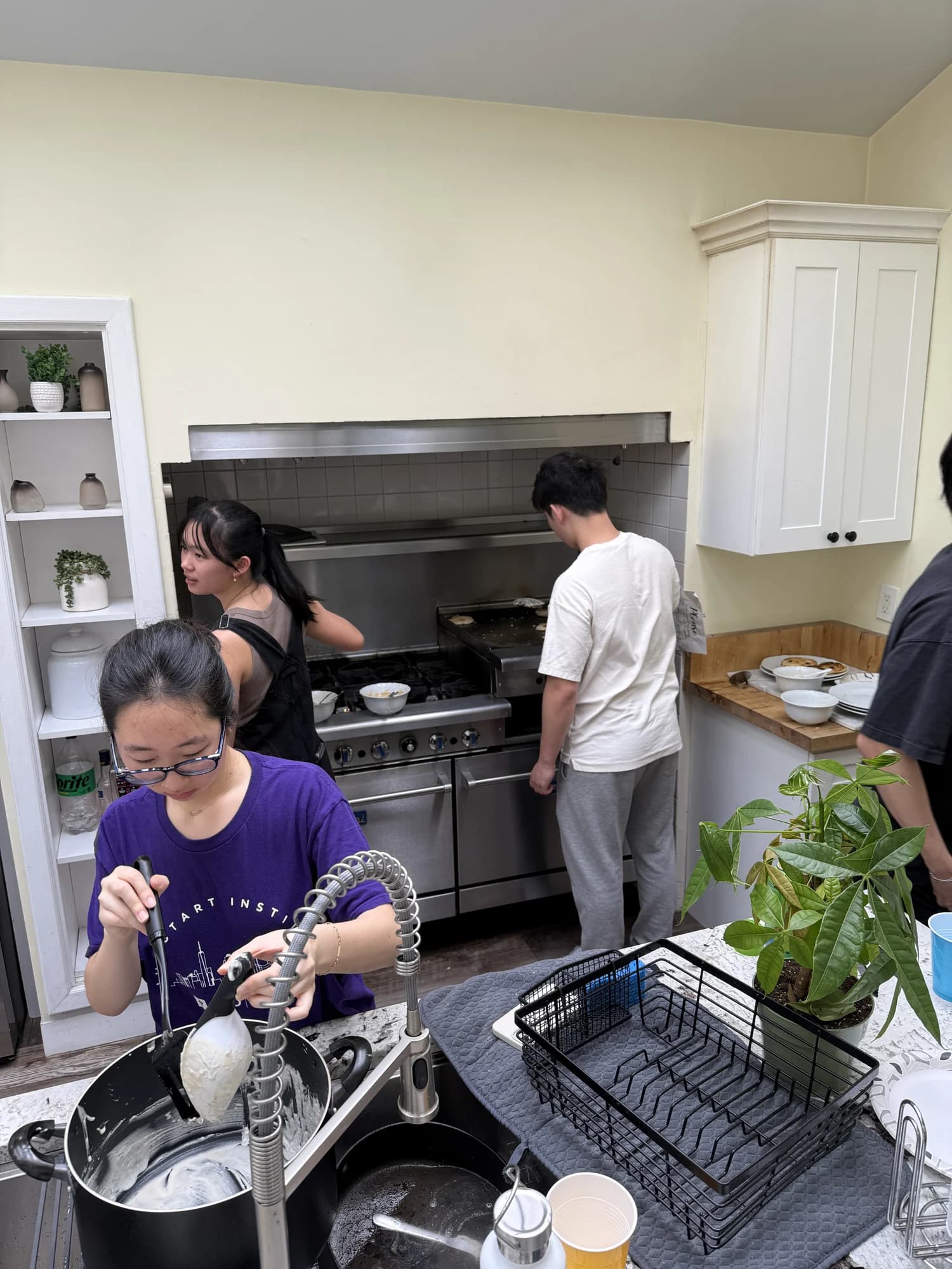 Three members cooking and washing up in a bright kitchen