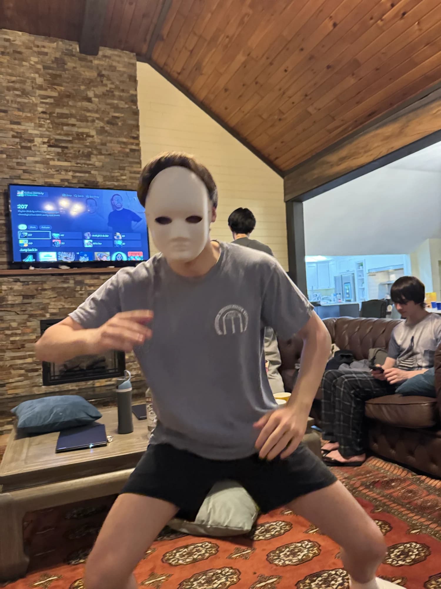 A member in a blank white mask striking a pose in a lodge living room