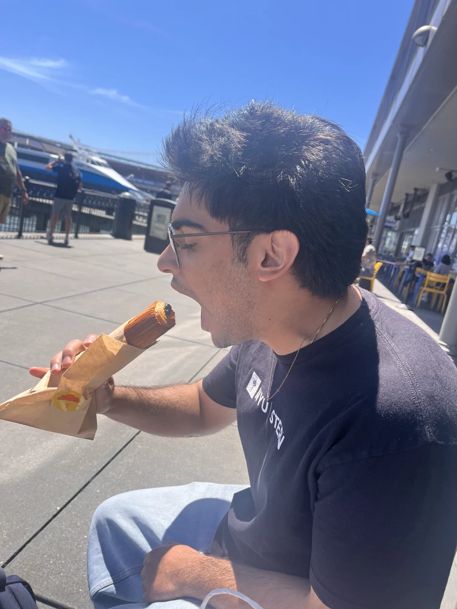 A member on a sunny pier, mid-bite into a hot dog
