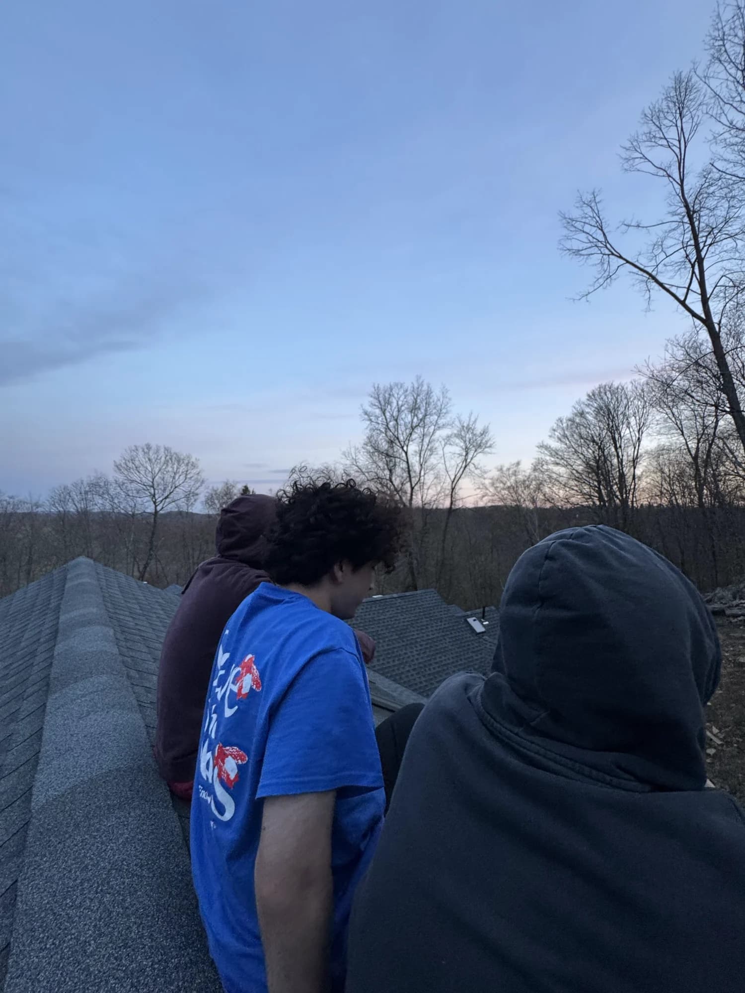 Three members sitting out on a shingled roof at dusk