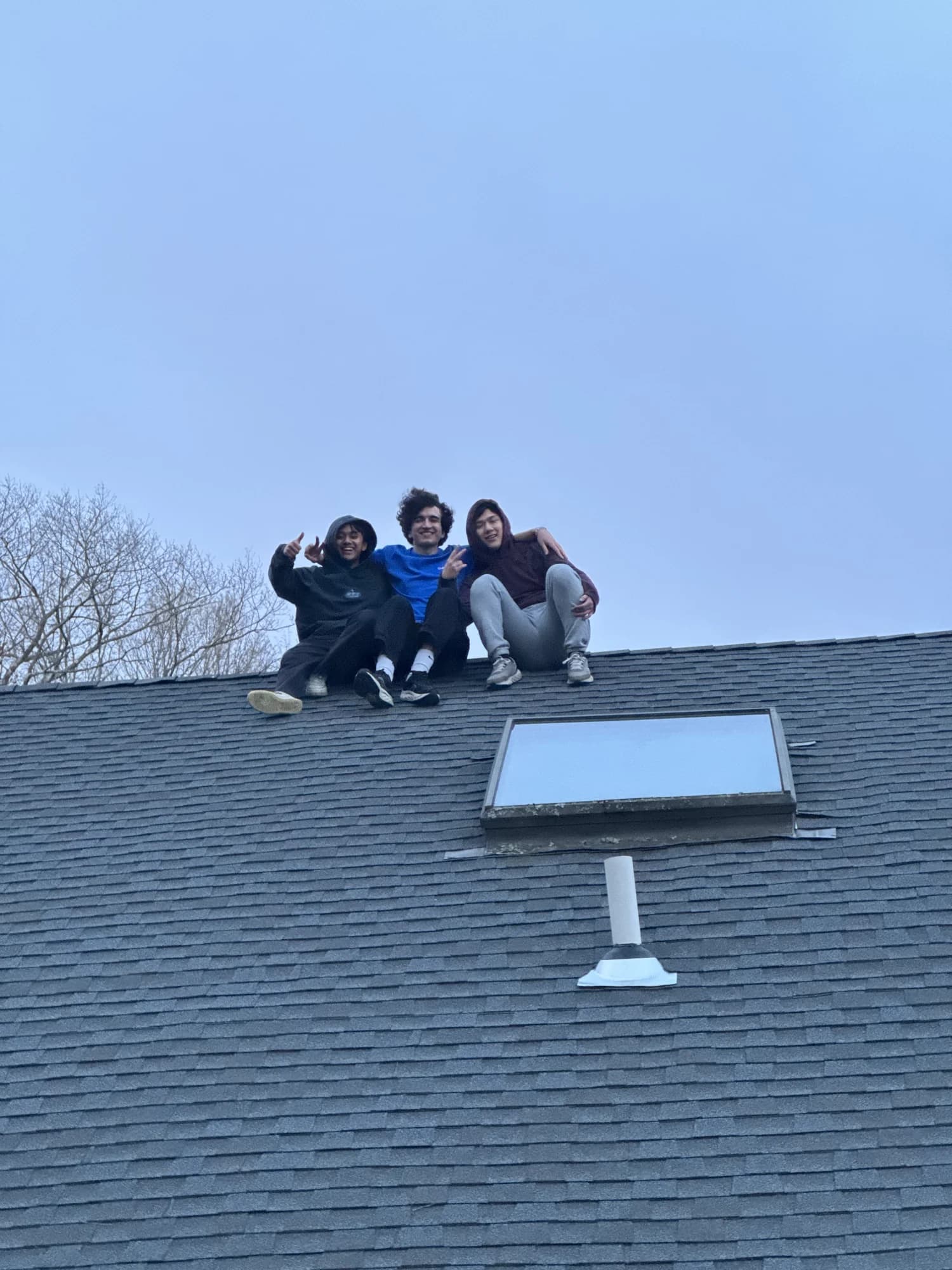 Three members perched on the peak of a roof, waving down