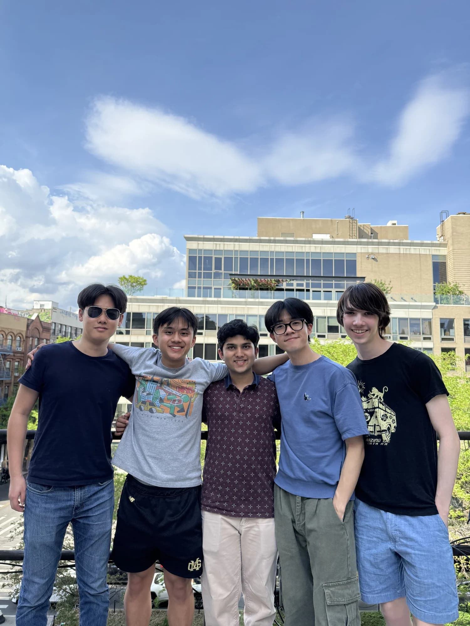 Five members shoulder to shoulder on a roof deck under a cloudy blue sky