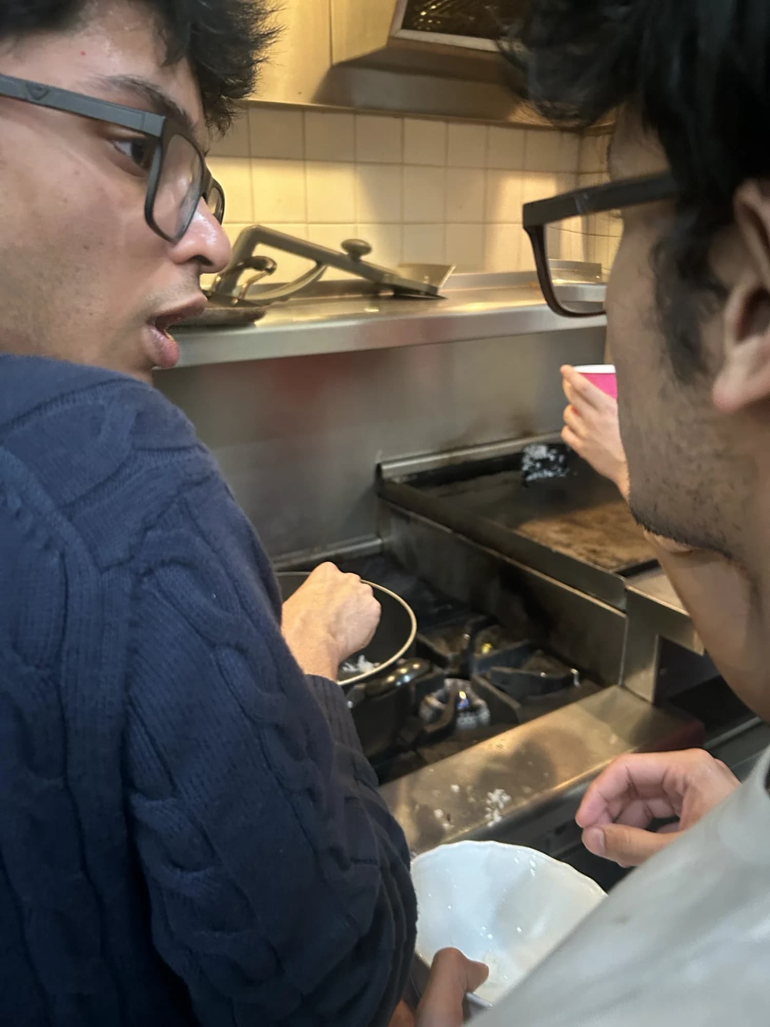 Two members close together at a stove, one mid-sentence