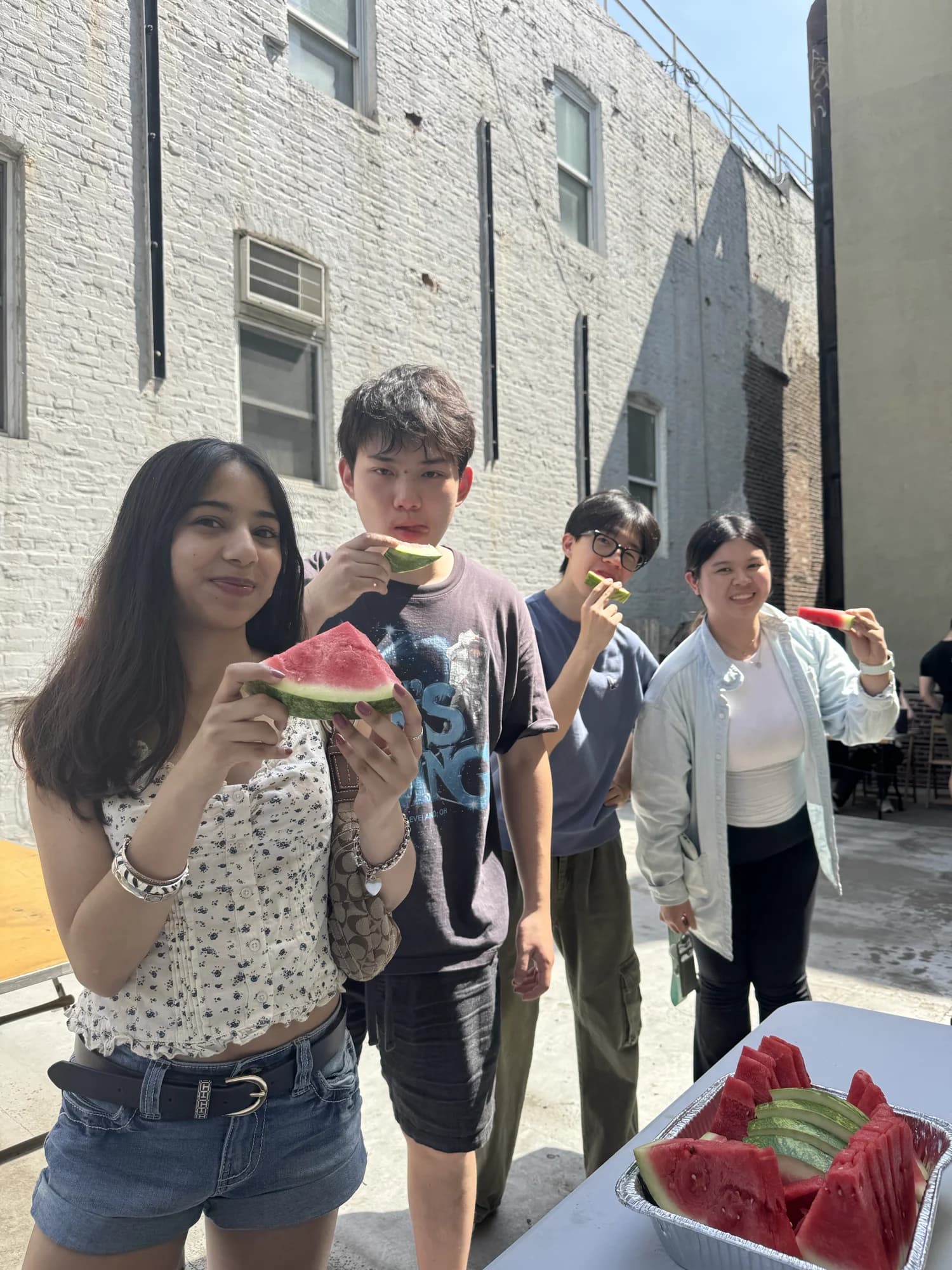 Four members eating watermelon in a backyard on a hot day